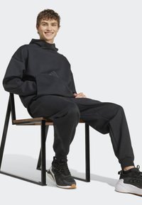 Black sweatshirt and sweatpants, made of soft fabric, with a relaxed fit, hood, and front pocket. Includes contrasting accents and sporty sneakers.