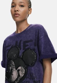 Fialové oversized bavlnené tričko s trblietavým čiernym dizajnom Mickey Mouse na prednej strane a textúrovanou látkou s opotrebovaným vzhľadom.