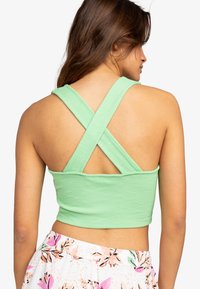 Groene geribbelde crop top met gekruiste rugbandjes, voorzien van een strakke pasvorm en een gladde textuur. Geen zichtbare versieringen of patronen.