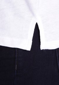 Vit bomullströja med en böjd öppning i kanten, kombinerad med mörkblå denim. Slät textur och klassisk design.