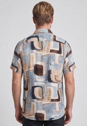 Mann trägt kurzärmliges Hemd mit abstraktem geometrischem Muster in Blau, Beige und Braun, von hinten vor neutralem Hintergrund gezeigt.