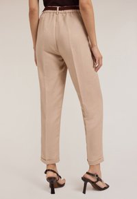 Helle beige, maßgeschneiderte Hose mit lässiger Passform, elastischem Bund und aufgerollten Säumen. Glatte Textur, flaches Frontdesign und keine sichtbaren Taschen.