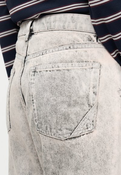 Ξεθωριασμένα γκρι τζιν τζιν με ψηλή μέση, που διαθέτουν πίσω τσέπη και εφέ ξεφτισμένου υφάσματος, κρατημένα από μια ριγέ σκούρα μπλε πουκάμισο.