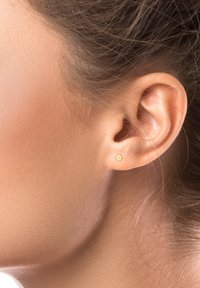 Gold stud earring featuring a smooth, round design, minimalistic texture, and a subtle sheen. Worn on the earlobe of a model.