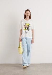 Hvit bomull t-skjorte med et leopardmotiv med neonlys, sammen med lyseblå vid bukser og en gul håndveske.