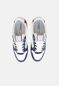 Zapatillas deportivas blancas y marinas con una superposición de ante texturizado, punta perforada y cordones blancos. Presentan acentos rojos y un logo en la lengüeta.