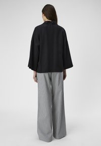 Top negro de corte holgado con mangas amplias, combinado con pantalones de pierna ancha a rayas de tiro alto. Tejido suave y silueta relajada.