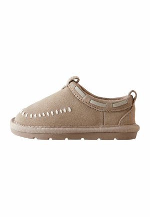 Chaussure beige à enfiler en daim, avec des coutures décoratives blanches, des tirettes et une semelle en caoutchouc épaisse et texturée, présentée de profil sur fond blanc.
