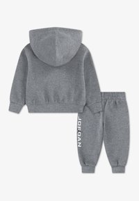 Harmaa hupullinen collegepaita ja siihen sopivat verkkarit, valmistettu pehmeästä kankaasta. Varustettu resorilla varustetuilla hihoilla, joustavalla vyötärönauhalla ja valkoisella "JORDAN"-tekstillä housuissa.