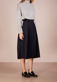 Pull à col roulé gris à manches longues, associé à une jupe midi plissée noire. Chaussures plates noires complètent la tenue. Design simple et élégant.