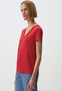 Rode shirt met korte mouwen en een V-hals, van een gladde stof, gecombineerd met lichtblauwe spijkerbroek. Eenvoudig ontwerp, zonder zichtbare patronen of accenten.