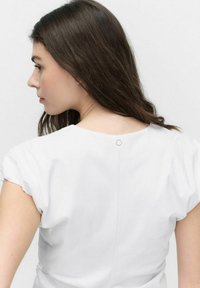 Witte blouse met korte, geraffineerde mouwen en een ronde sluiting aan de achterkant van de nek, met een gladde stoftextuur en een minimalistisch ontwerp.