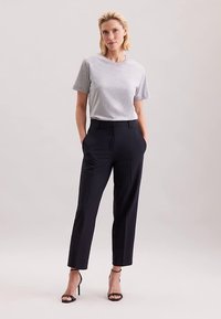 Grå t-shirt med korte ærmer kombineret med skræddersyede sorte bukser med folder foran og slank pasform. Modellen står i sandaler med ankelremme.