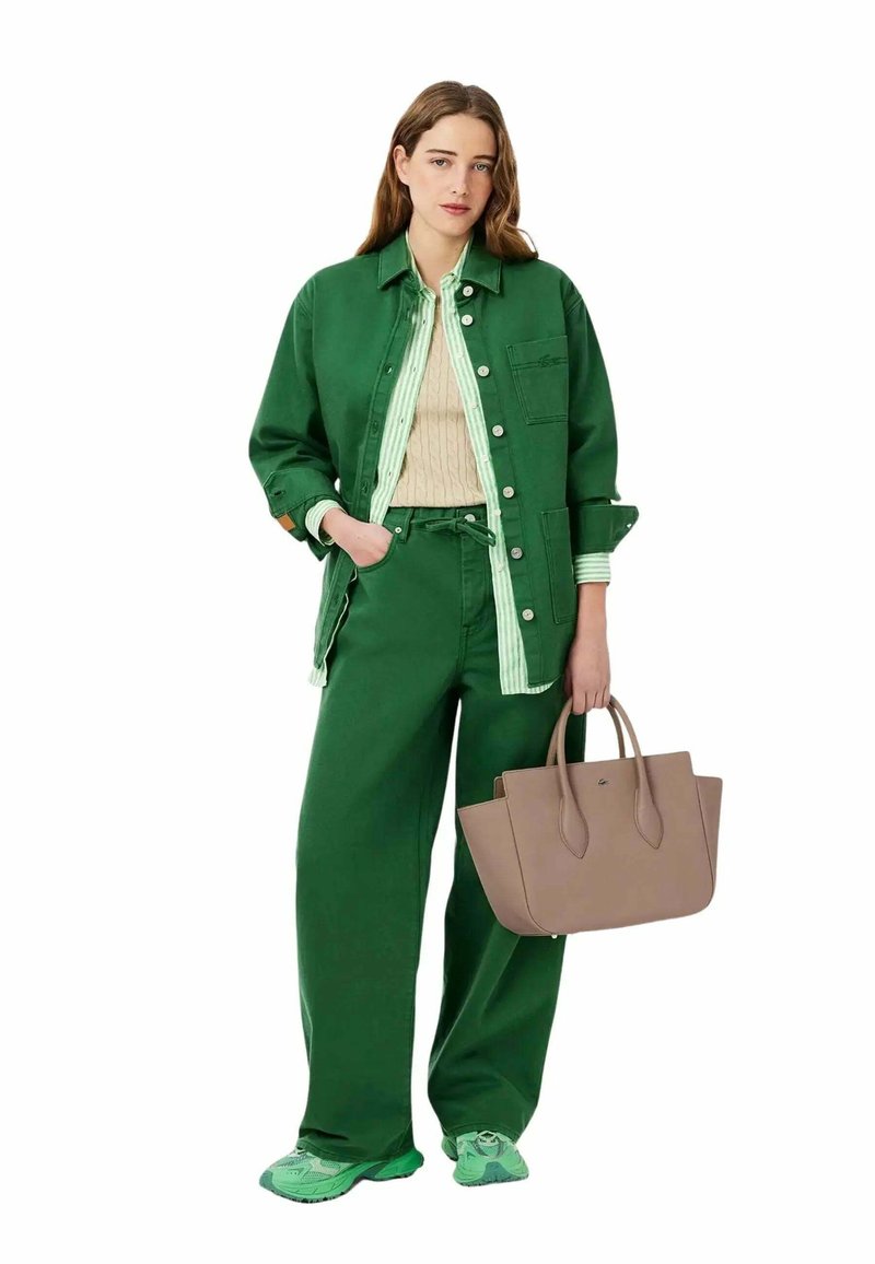 Veste en denim vert sur un pull vert avec des accents rayés, associée à un pantalon vert à jambes larges et un sac fourre-tout marron clair. Des baskets vertes complètent le look.