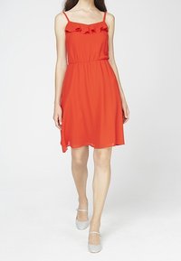 Rotes ärmelloses Kleid mit Rüschendetail am Ausschnitt, elastischem Bund und einem fließenden Rock. Getragen mit hellgrauen Ballerinas.