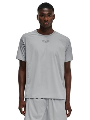 Mężczyzna ubrany w jasnoszary sportowy t-shirt z krótkim rękawem i pasujące szorty, stojący na białym tle.