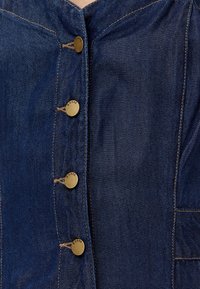 Tessuto di denim blu scuro con righe verticali, caratterizzato da cinque bottoni dorati sulla parte anteriore e dettagli di cucitura visibili.