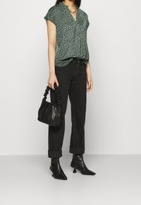 Blusa corta a maniche corte con stampa leopardata verde, jeans neri a vita alta, stivaletti neri con tacco e una piccola borsa nera in tessuto texture.