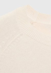 Pull en tricot couleur crème clair avec un col rond à côtes, des détails texturés sur les épaules et une finition en tissu doux et lisse.