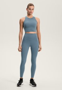 Modra športna kratka majica in hlače z visokim pasom iz raztegljivega materiala, z gladko teksturo in oprijetim dizajnom, kombinirana s črnimi supergami.