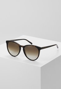 Ochelari de soare cu ramă din plastic cu model țestoasă și lentile maronii cu gradient. Prezintă o formă rotundă de tip cat-eye și accente aurii discrete.