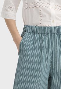 Pantalon à rayures bleu clair avec une ceinture élastique et des poches latérales, assorti à une chemise blanche à œillets boutonnée.