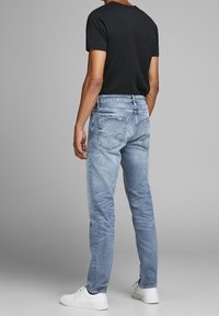 Ljust blå denimjeans med rak passform, blekning på låren, fem fickor och sydda detaljer. Matchas med en svart t-shirt och vita sneakers.