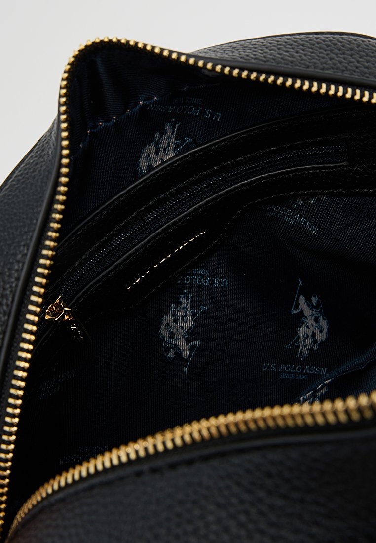 Intérieur d'un sac en cuir noir avec une fermeture éclair dorée ; présente une doublure en tissu à motifs navy avec des logos de polo bleus et des détails textuels.