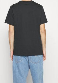 Camiseta de algodón negra con cuello redondo, mangas cortas y corte recto, combinada con vaqueros de corte holgado en azul claro.