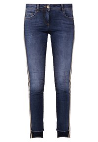 Jeans de mezclilla de un azul oscuro con franjas laterales. Presentan un diseño clásico de cinco bolsillos, cierre de botón y dobladillos deshilachados. Corte ajustado.