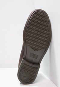 Bruine suede schoen met een gestructureerde rubberen zool met een zigzagpatroon, geperst logo en rondneus ontwerp. Zool is plat en breed.