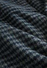 Wollstoff in dunkelblau und grauem Hahnentrittmuster, strukturierte Oberfläche mit einem weichen, flauschigen Aussehen, das Wellen und Falten zeigt.