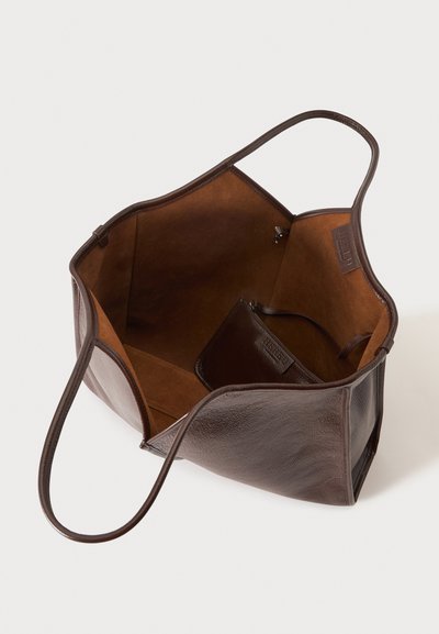 Sac cabas en cuir marron foncé ouvert avec une petite pochette assortie à l'intérieur sur fond blanc.