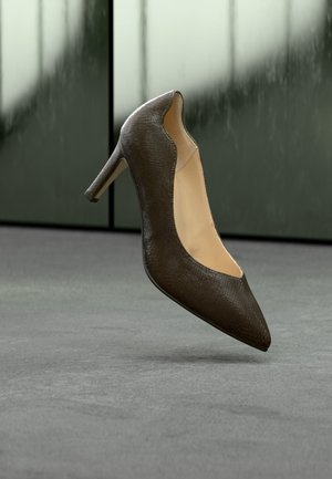 Dunkelbrauner, strukturierter Leder-High-Heel-Schuh mit spitzer Spitze, schwebend über einem grauen Boden vor satinierten Glasplatten.
