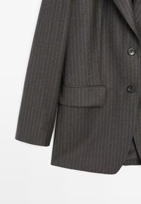Donkergrijs gestreepte blazer met een notch lapel, een enkelvoudig ontwerp, twee knopen en een zijzak. Gelaagde stof met blauwe strepen.