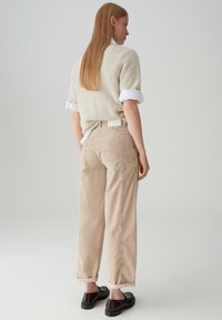 Pantaloni in corduroy beige con una vestibilità larga, orli arrotolati e grandi tasche posteriori, abbinati a un maglione chiaro e texturizzato.