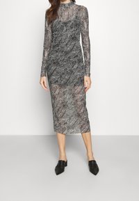 Pitkähihaisessa, läpikuultavassa musta-valkoisessa mekossa on lehtikuvio ja rypytys. Midi-pituinen, vartalonmyötäinen muotoilu ja korkea kaula-aukko.