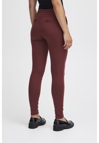 Vinröda leggings med elastisk midja, med två bakfickor. Bärs med svarta lackskor, slät textur och smal design.