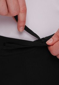 Black adjustable waistband with a drawstring. Material appears smooth and stretchy. A hand grips the drawstring inside the waistband.