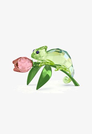 Figurka kameleona z kryształu w zielonym kolorze z niebieskimi oczami, trzymająca różowy kryształowy kwiat. Charakteryzuje się gładkimi, fasetowanymi powierzchniami i zakrzywionymi liśćmi.