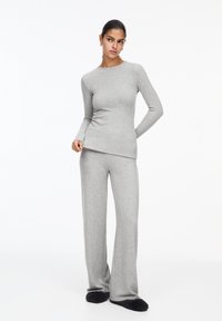 Maglia grigia a maniche lunghe in maglia con pantaloni a gamba larga coordinati in morbido tessuto, caratterizzati da scollatura rotonda e polsini aderenti, abbinati a pantofole nere.