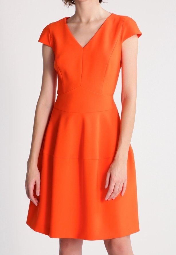 Femme portant une robe orange vif à manches courtes et encolure en V, taille cintrée et jupe évasée, sur un fond uni.