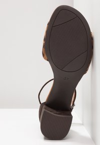 Sandale à talon en daim marron avec un talon block et une tige à motifs. Semelle en caoutchouc texturé avec des rainures pour une bonne adhérence. Taille 37 indiquée sur la semelle.