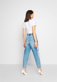 Jeans azzurri chiari a vita alta con una vestibilità comoda, caratterizzati da un lavaggio sbiadito, cinque tasche e un design a gamba dritta, indossati con una maglietta bianca e tacchi.