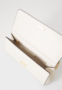 Sac à main en cuir beige avec un design structuré. Il présente des quincailleries en accent doré, une texture lisse et un compartiment intérieur zippé.