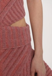 Top corto in maglia e gonna in una morbida tonalità rosa, con motivi a coste e diagonali, finitura testurizzata e pelle esposta in vita.