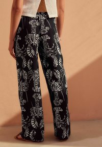 Pantalon large noir avec un motif de plantes blanches et abstrait, fabriqué à partir d'un tissu léger. Taille élastique et coupe décontractée.