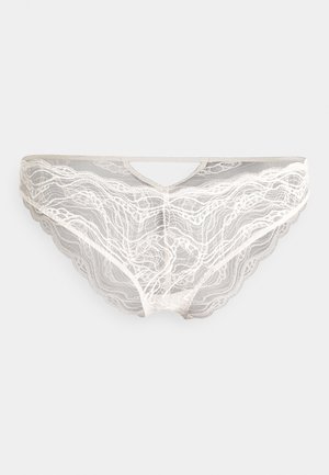 Lace undertøy i lys beige med bølgemønster, bølget kant, og en V-formet utskjæring foran. Myk, gjennomsiktig tekstur gjennom hele.
