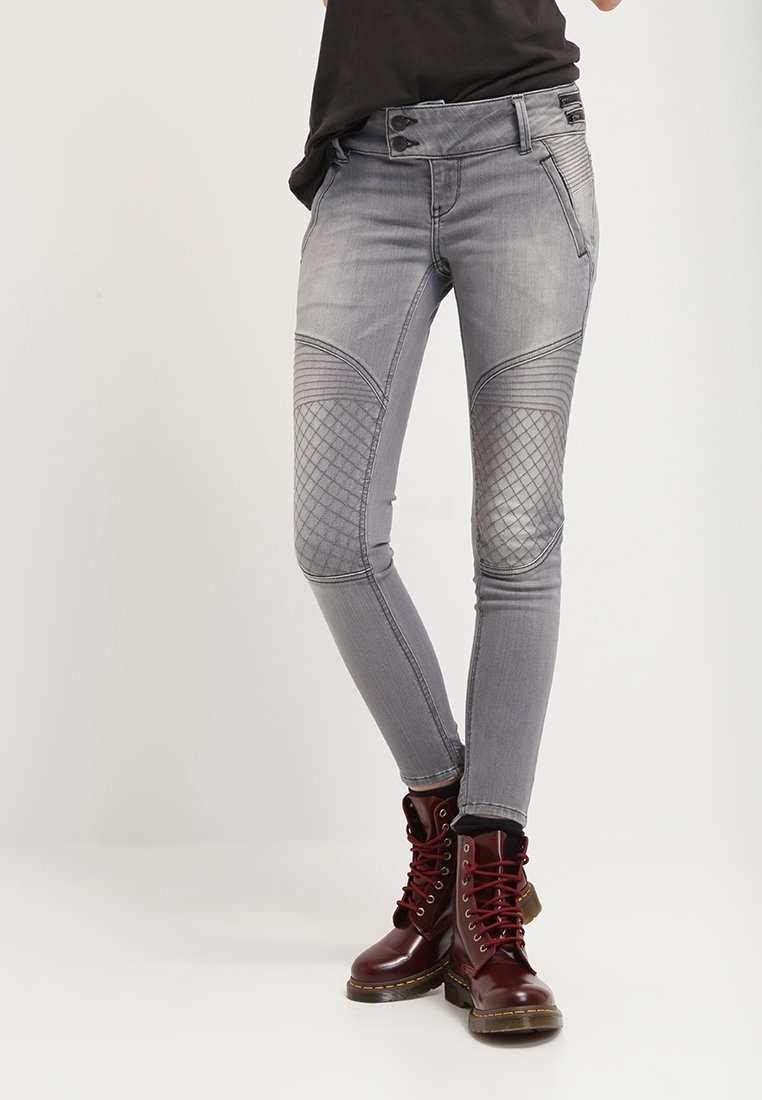 Jeans gris ajustados con paneles texturizados en las rodillas y costuras decorativas. Combinados con botas de combate burdeos con cordones.