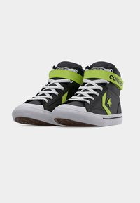 Μαύρα ψηλά αθλητικά παπούτσια Converse με λευκά κορδόνια, φουξια πράσινο λουράκι και λογότυπο αστέρι, και λευκές ελαστικές σόλες.